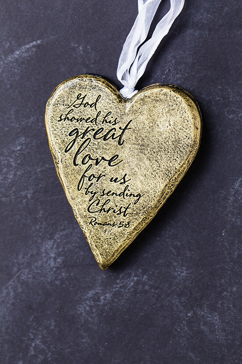 Romans 5:8 verse in script on a heart ornament