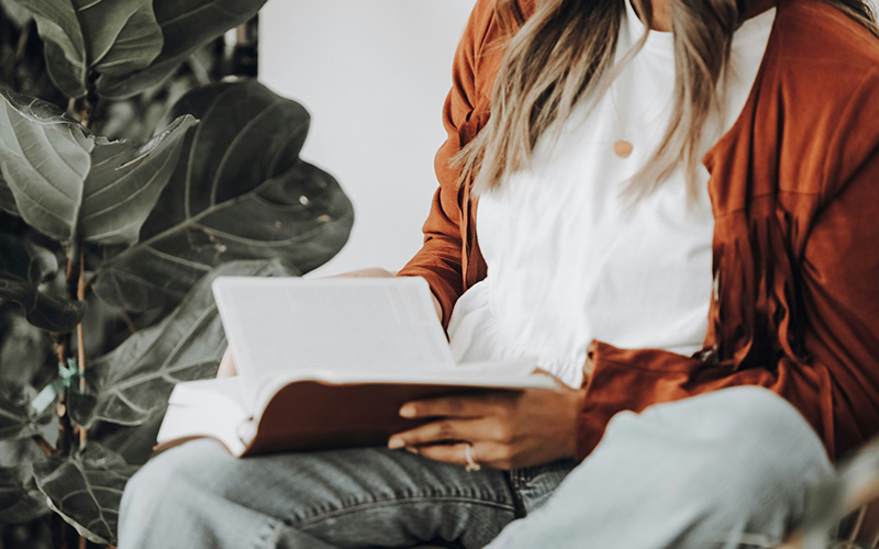 Bible Verses to Read in the Morning - Main Image - woman wearing jeans and a sweater holding a open bible on her lap