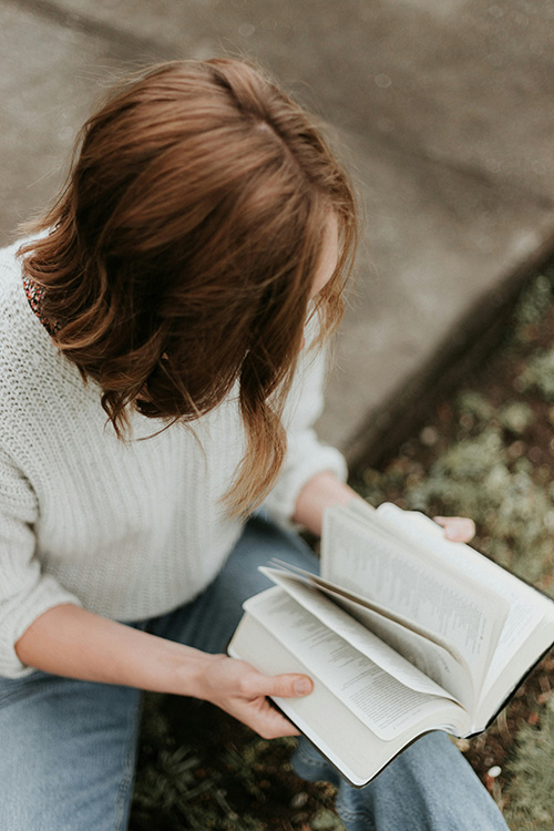 Woman sitting outdoors on a step flipping through a bible