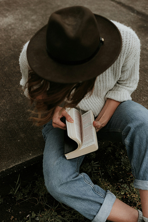 woman wearing a hat holding a bible on her lap flipping the pages