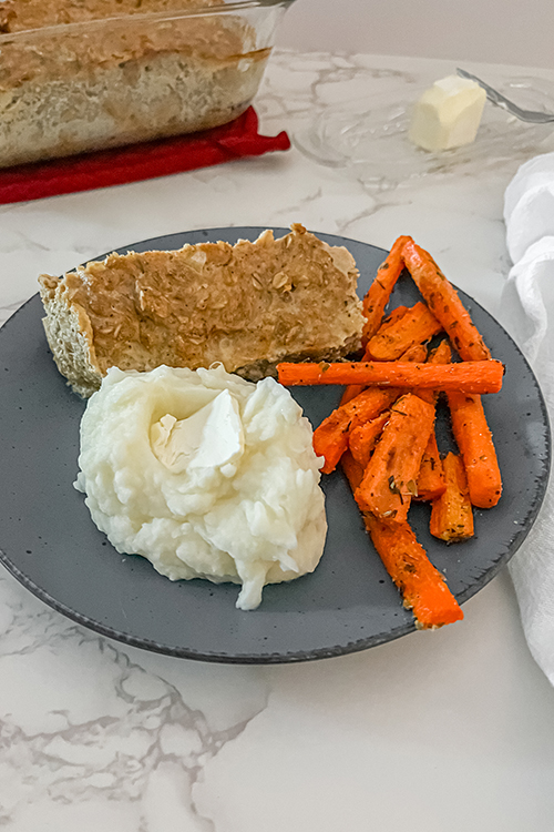 Finished meatloaf on a plate with buttered mashed potatoes and roasted carrots
