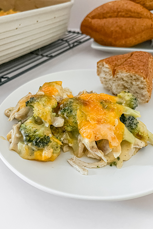 close up of chicken and broccoli casserole on a plate with a whole grain roll