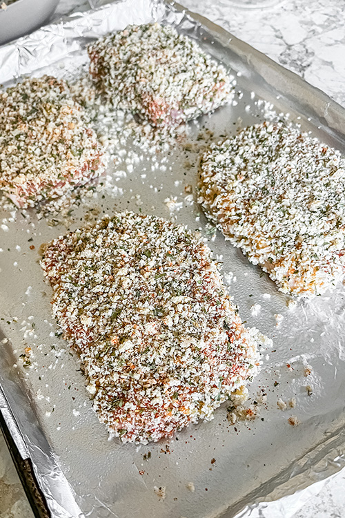 breaded pork chops on a lined sheet pan ready to bake