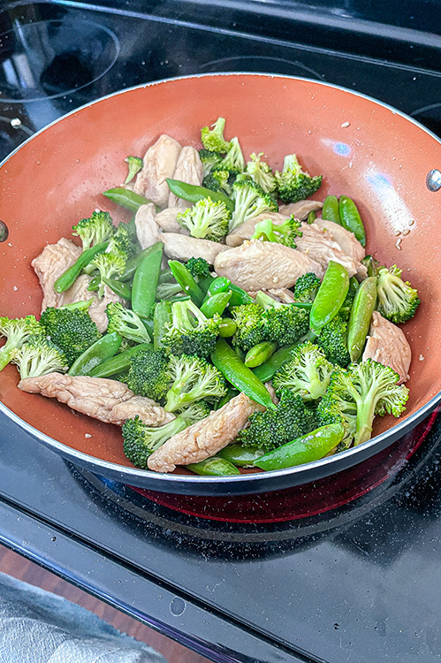 wok full of chicken strips and broccoli and snap peas