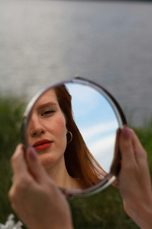 woman looking at her reflection in a handheld mirror with a straight face