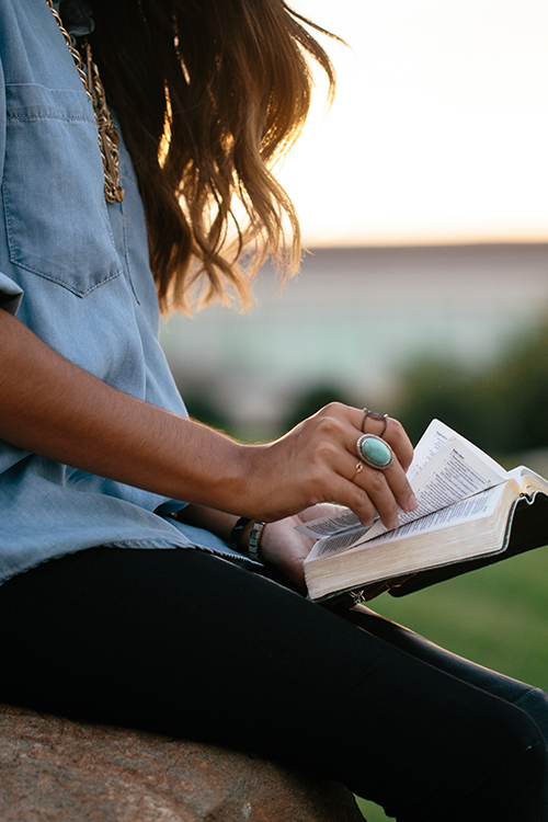 woman with long dark hair and an open bible on her lap outdoors, for bible verses on identity and purpose blog post